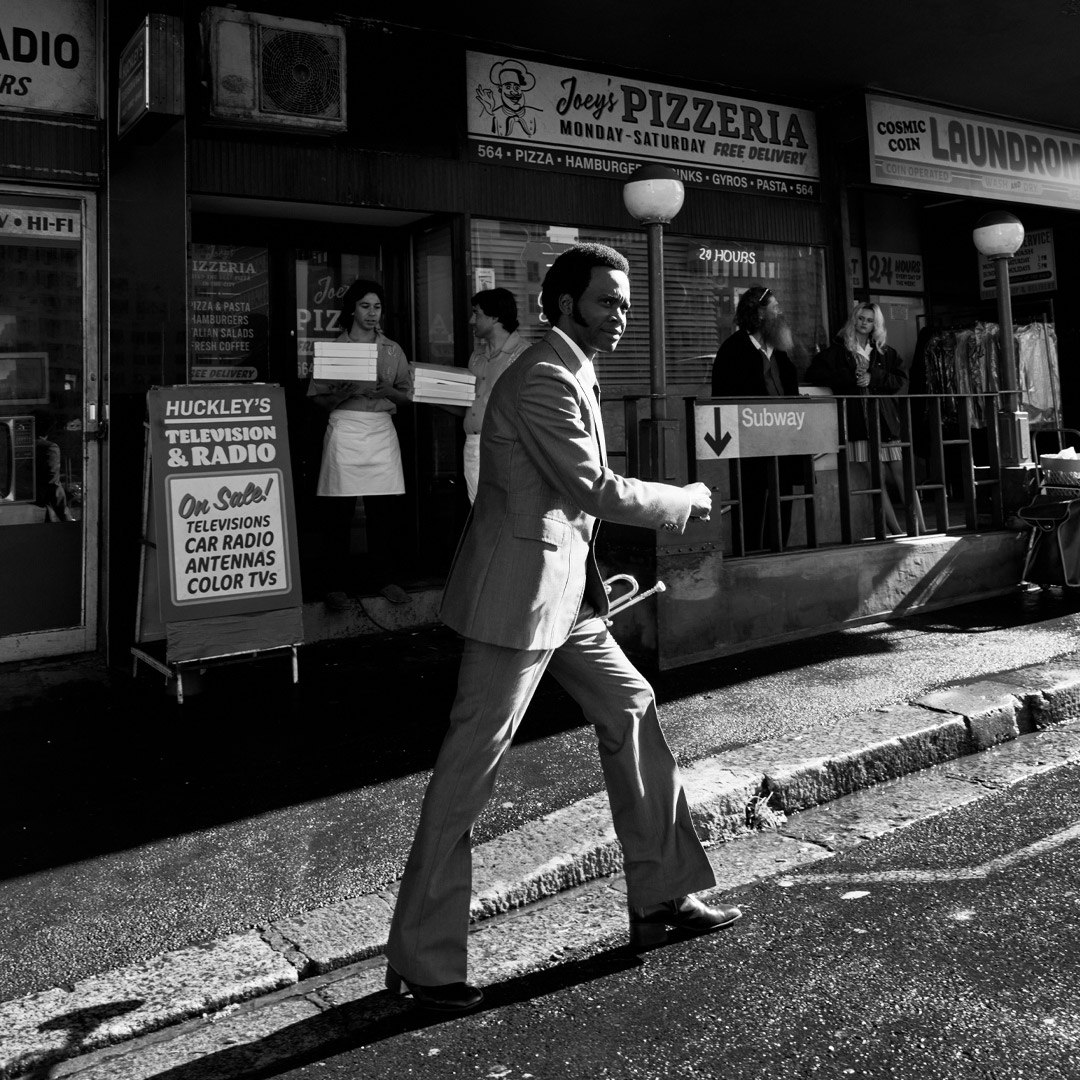 Grayscale photo of same older musician crossing the street 