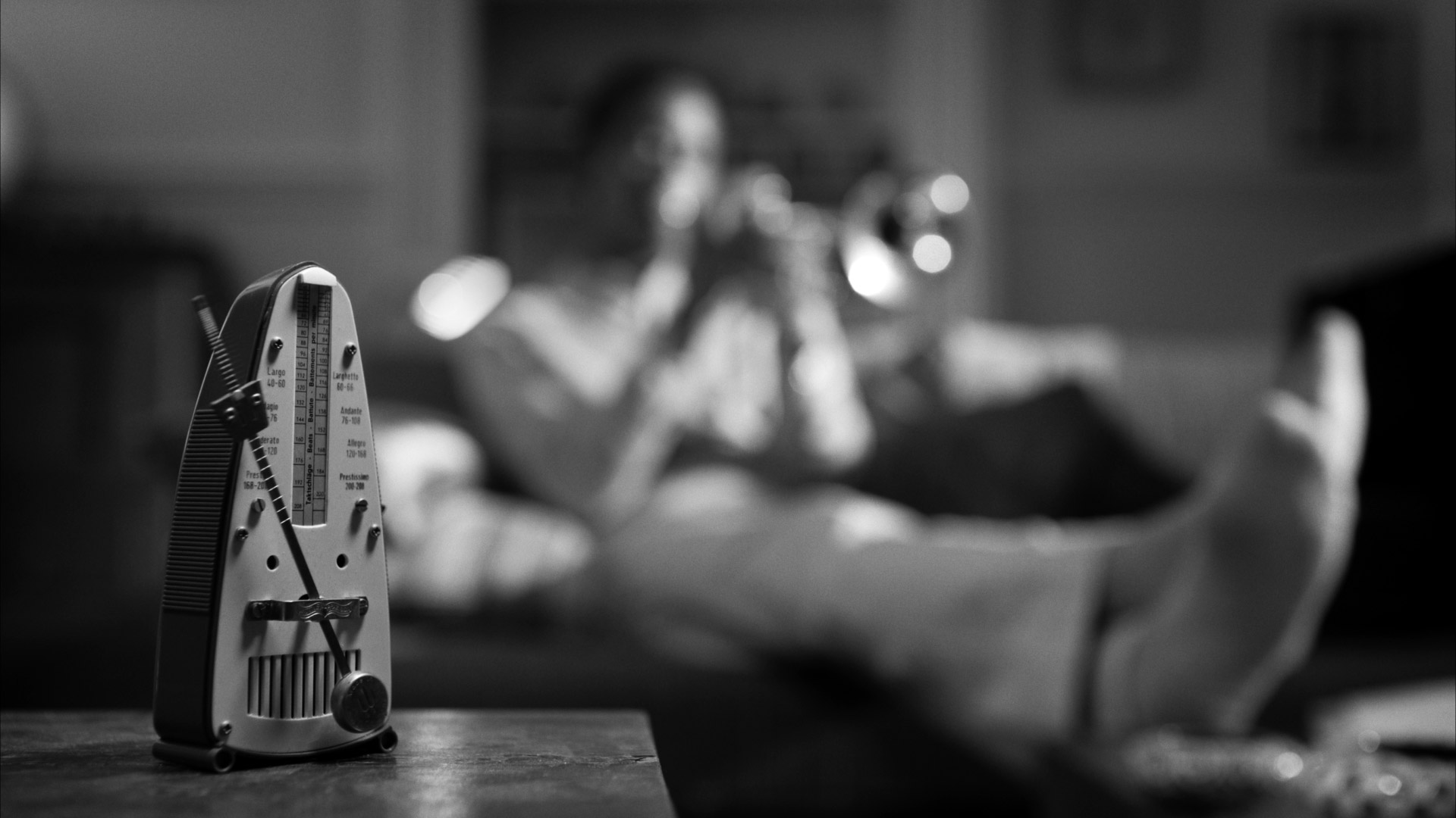 Grayscale background of a metronome on a table and a non-descript man playing a trumpet